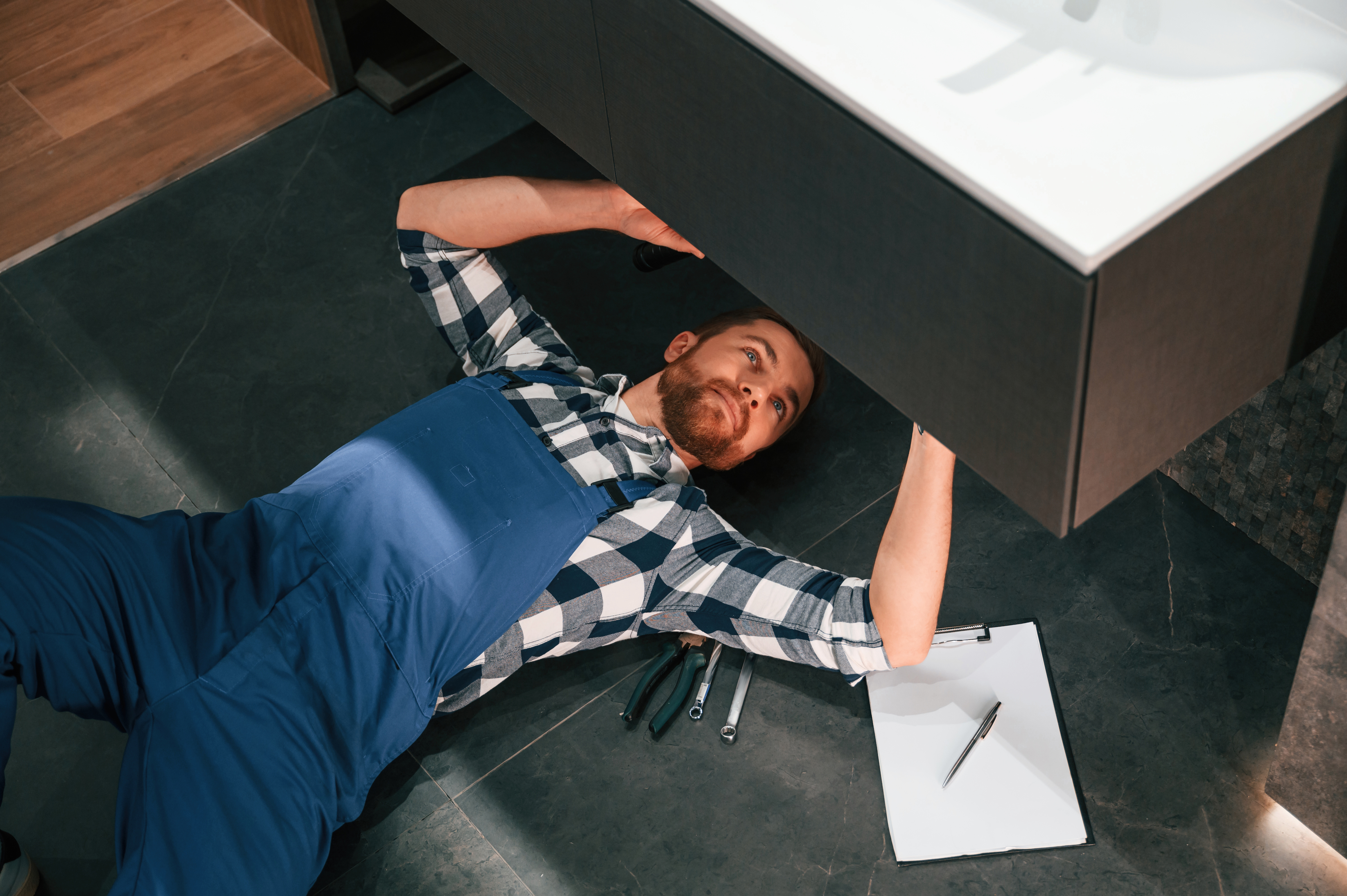 Plombier répare évier sous lavabo, outils à côté.